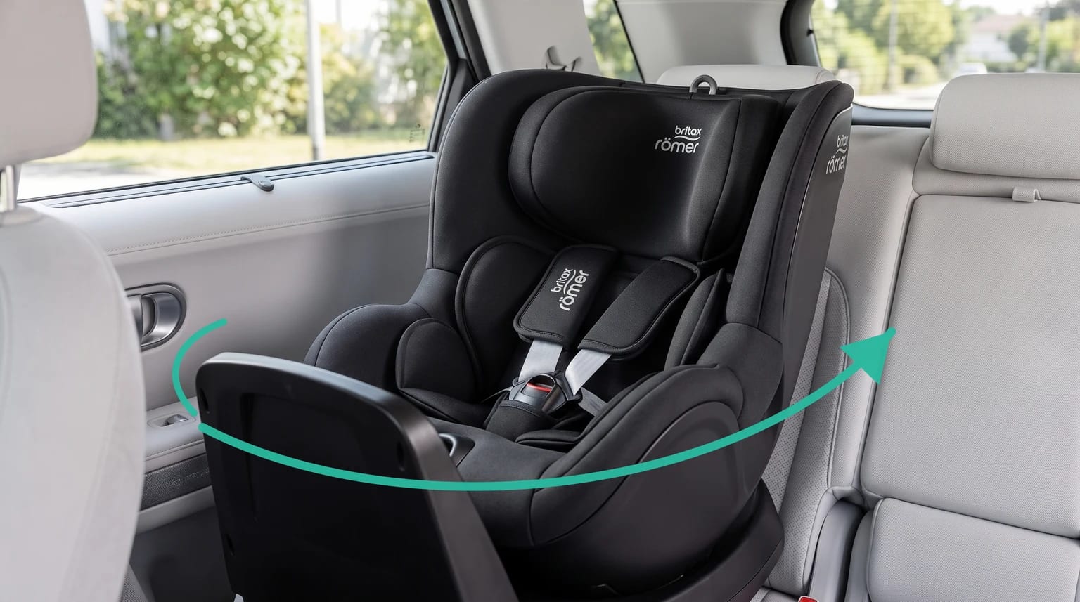 Silla de coche Britax Römer DUALFIX PLUS negra instalada en el asiento trasero de un coche con tapicería gris claro y una flecha verde que indica el giro.