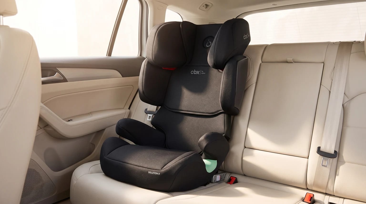 Silla de coche elevadora con respaldo de color negro, instalada en el asiento trasero de un coche con tapicería clara.