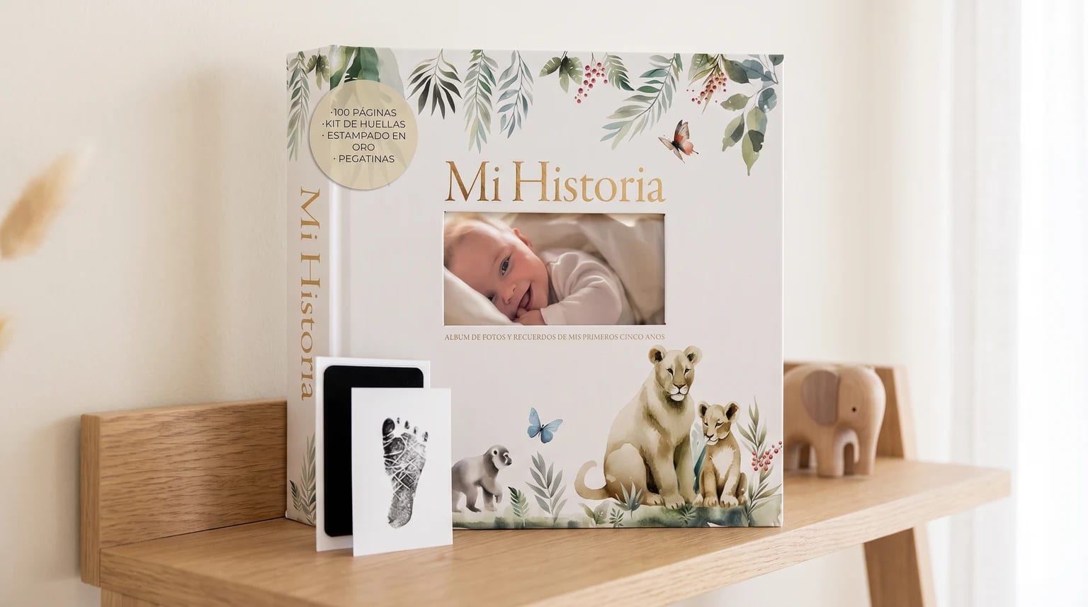 Álbum de recuerdos de bebé 'Mi Historia' con ilustraciones de acuarela, junto a un kit para huellas, sobre una estantería de madera.