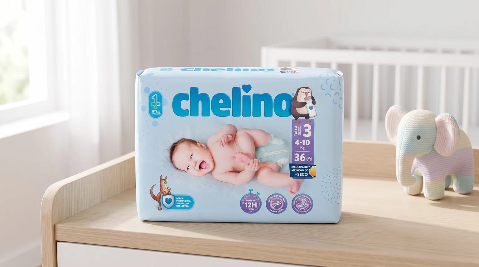 Un paquete de pañales Chelino sobre un cambiador de madera, al lado de un elefante de juguete tejido y con una cuna blanca al fondo.