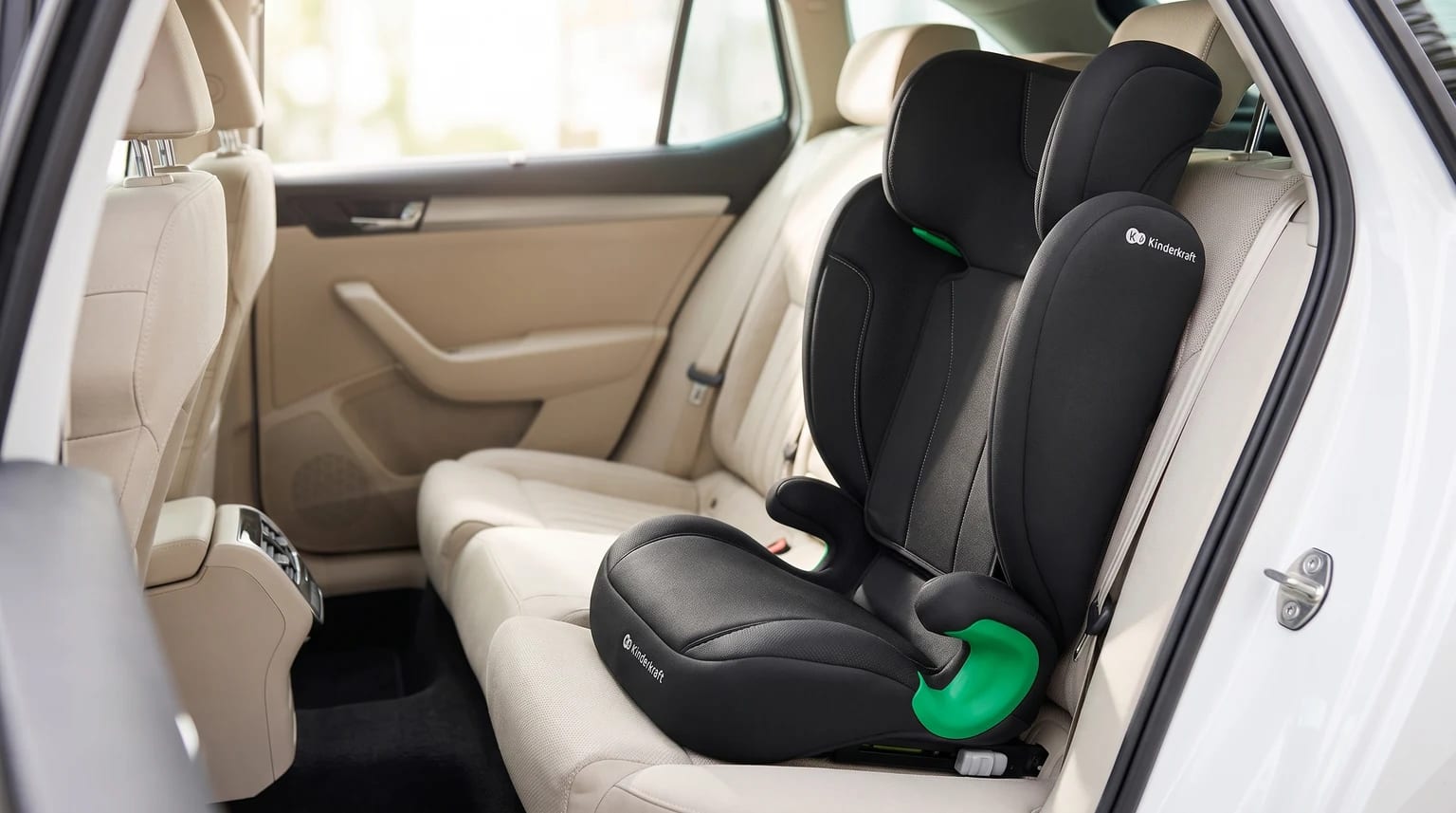 Silla de coche elevadora negra con detalles en verde, instalada en el asiento trasero de un vehículo con tapicería de color beige.