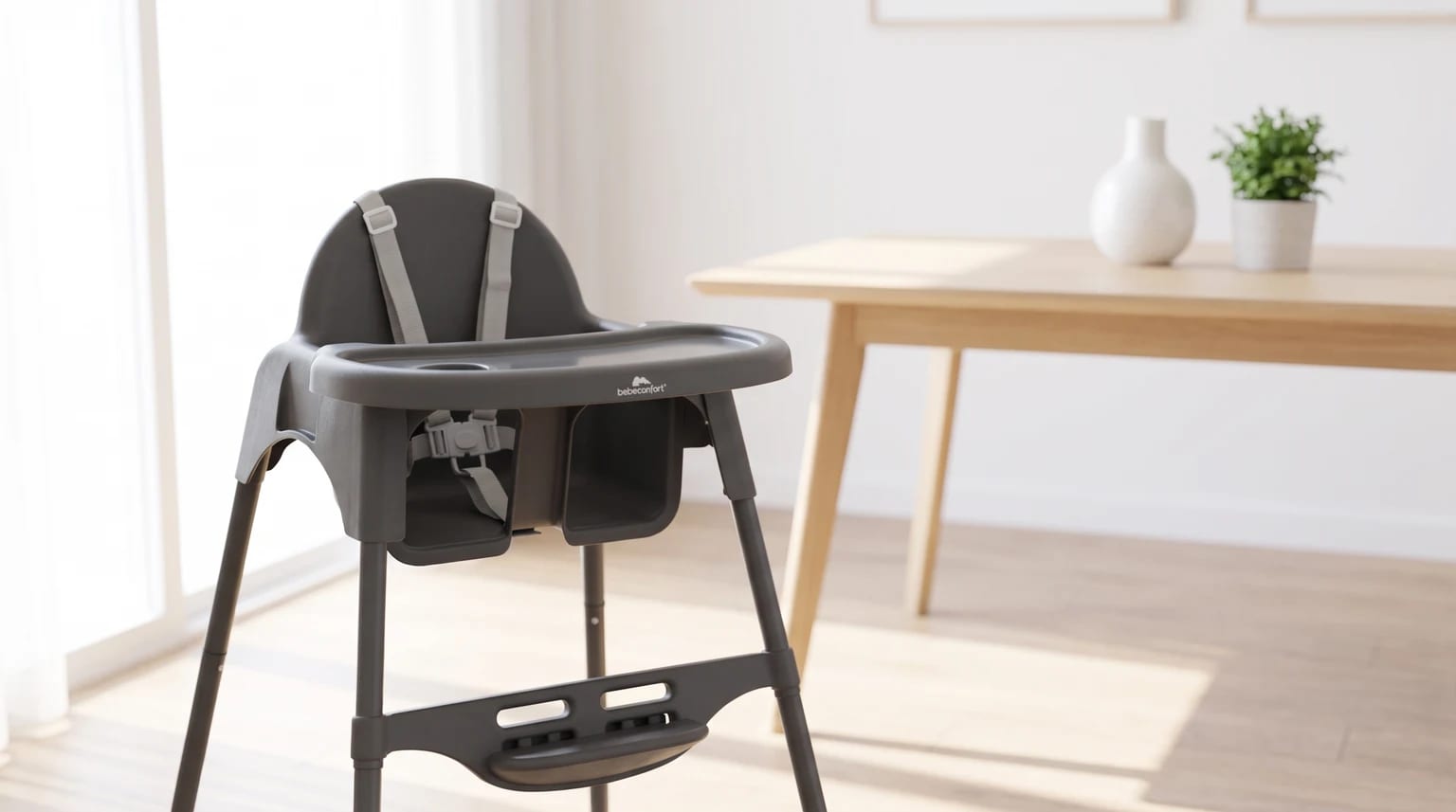 Trona alta de color gris oscuro colocada en un comedor luminoso junto a una mesa de madera clara.