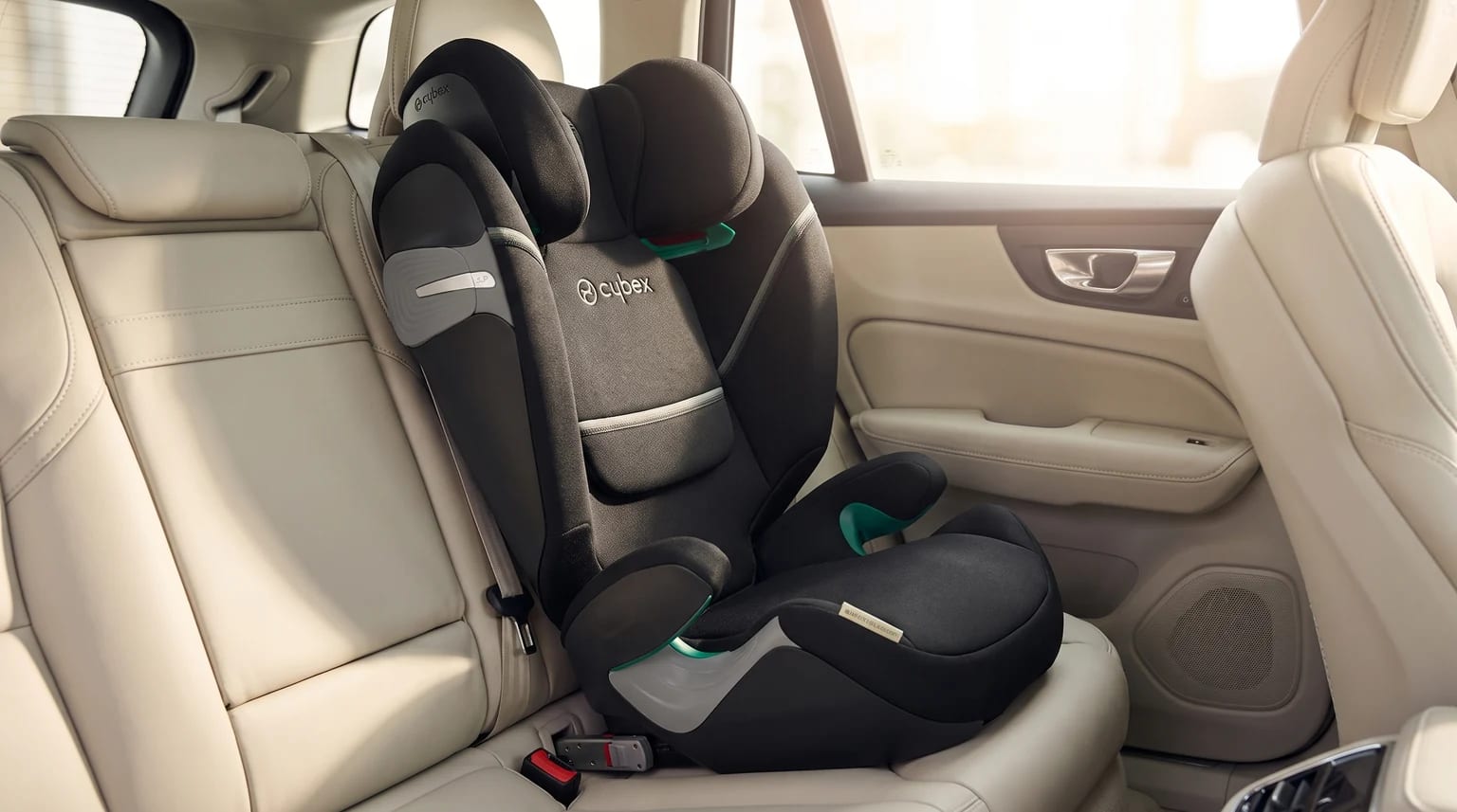 Silla de coche Cybex negra y gris instalada en el asiento trasero de un coche con tapicería de cuero color crema.