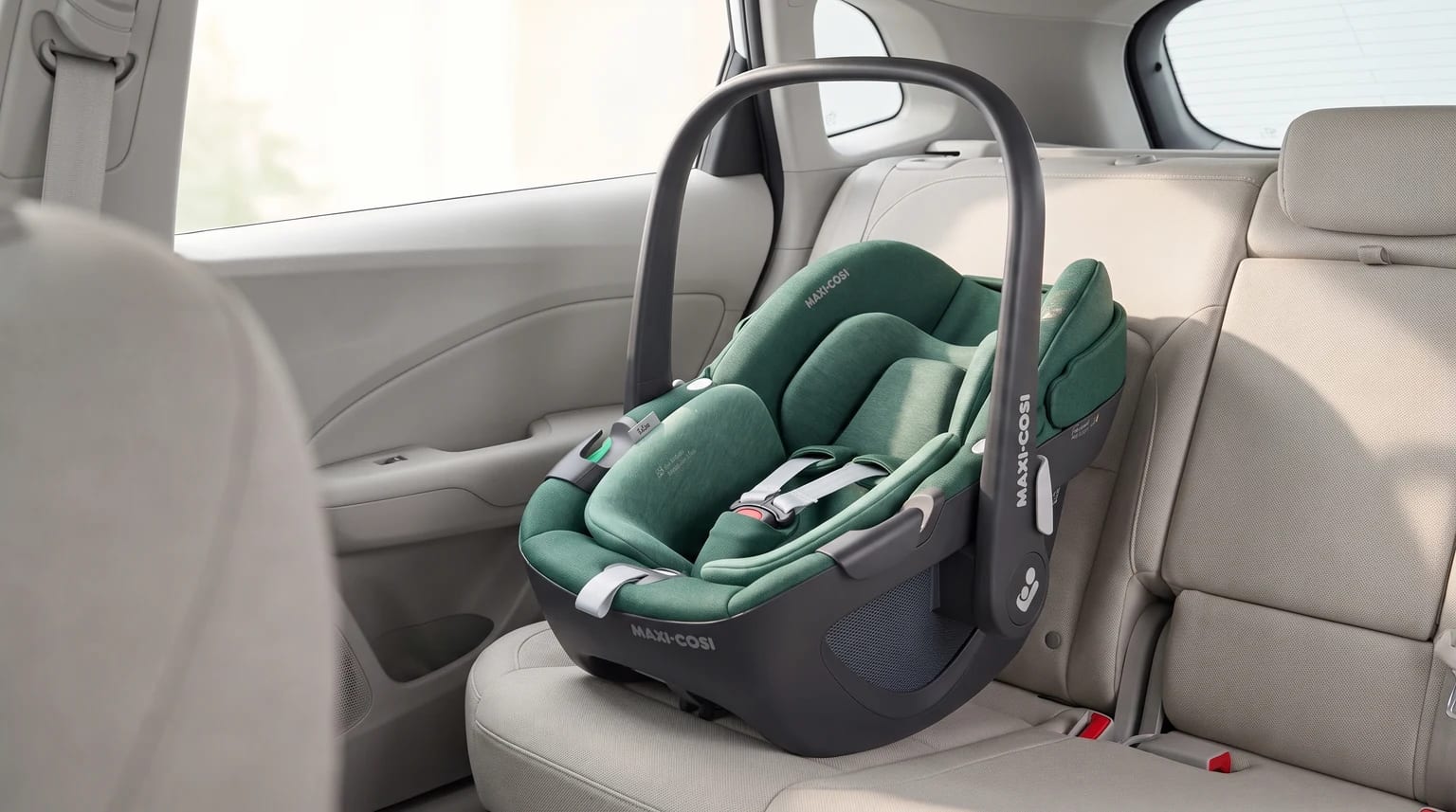 Portabebés Maxi-Cosi Pebble 360 verde colocado en el asiento trasero de un coche con tapicería beige.