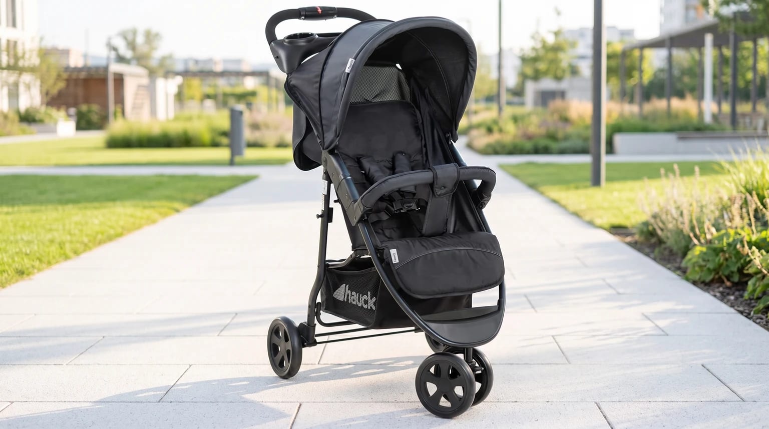 Silla de paseo hauck Citi Neo II negra sobre un camino de baldosas en un parque moderno.