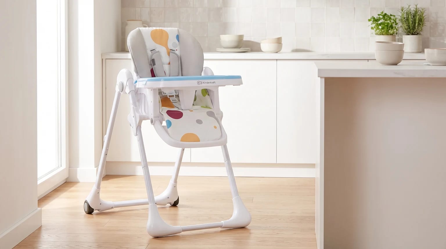 Trona blanca con un cojín estampado de círculos de colores, colocada sobre el suelo de madera de una cocina luminosa.