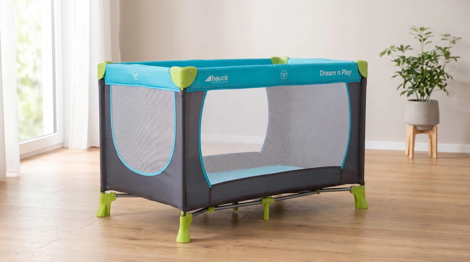 Cuna de viaje gris y turquesa con detalles en verde lima, montada en una habitación luminosa con suelo de madera.