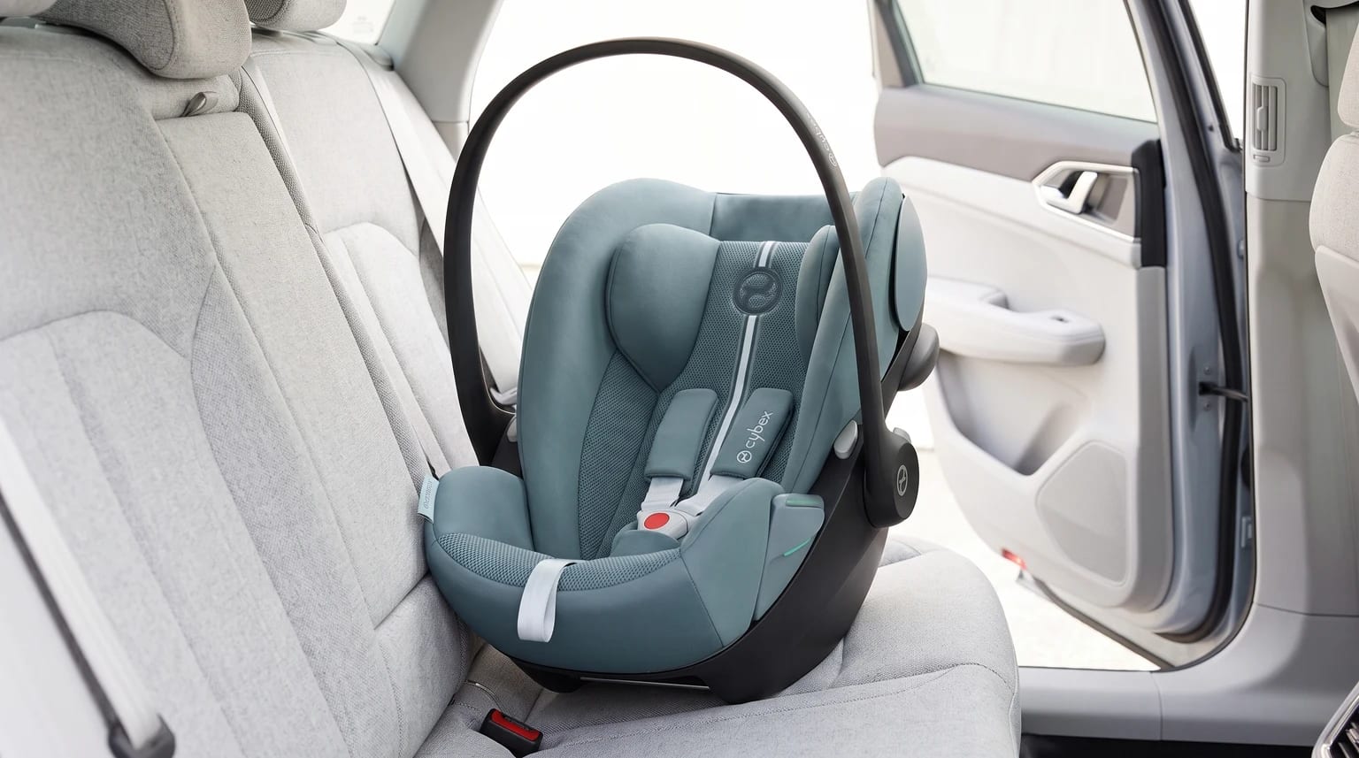 Portabebés Cybex Cloud G verde azulado colocado en el asiento trasero de un coche con tapicería gris claro.