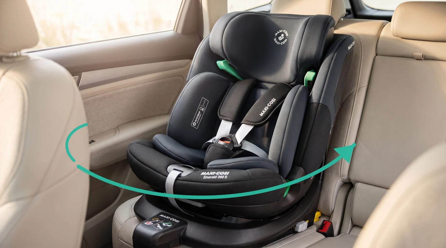 Silla de coche Maxi-Cosi Emerald 360 S de color negro, instalada en el asiento trasero de un coche con tapicería clara y una flecha verde que indica el giro.