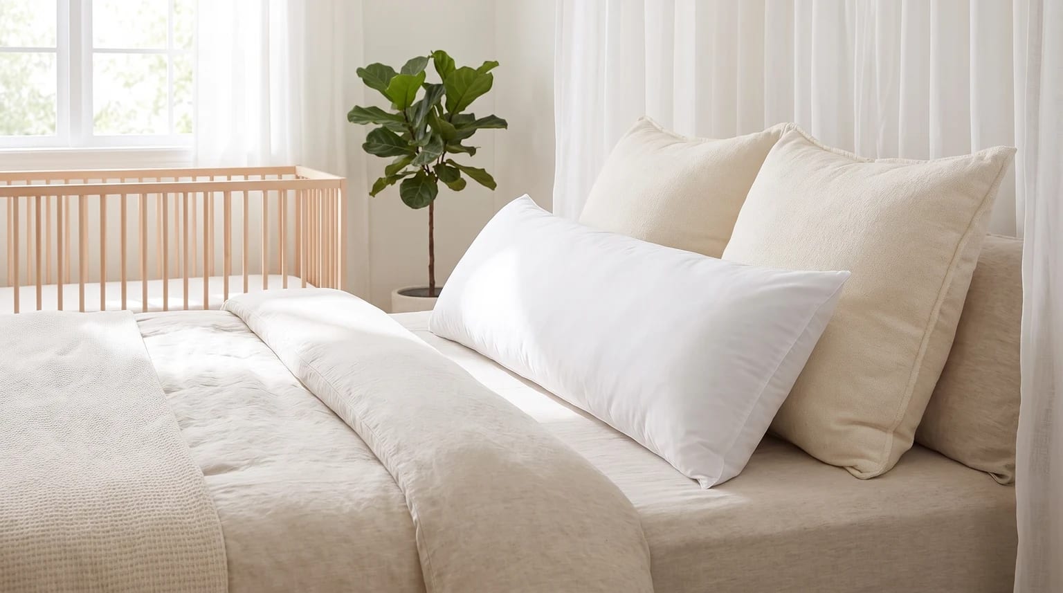 Almohada corporal blanca y alargada sobre una cama con sábanas de color neutro en un dormitorio luminoso.