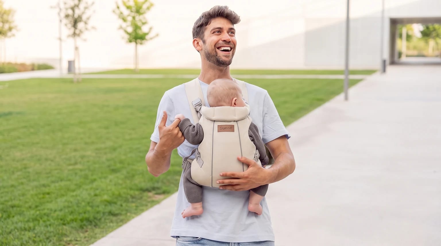 Un padre sonriente pasea al aire libre llevando a su bebé en una mochila portabebé de color beige.
